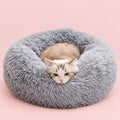 Grey faux fur donut pet bed with a cat curled up inside, on a blush pink background