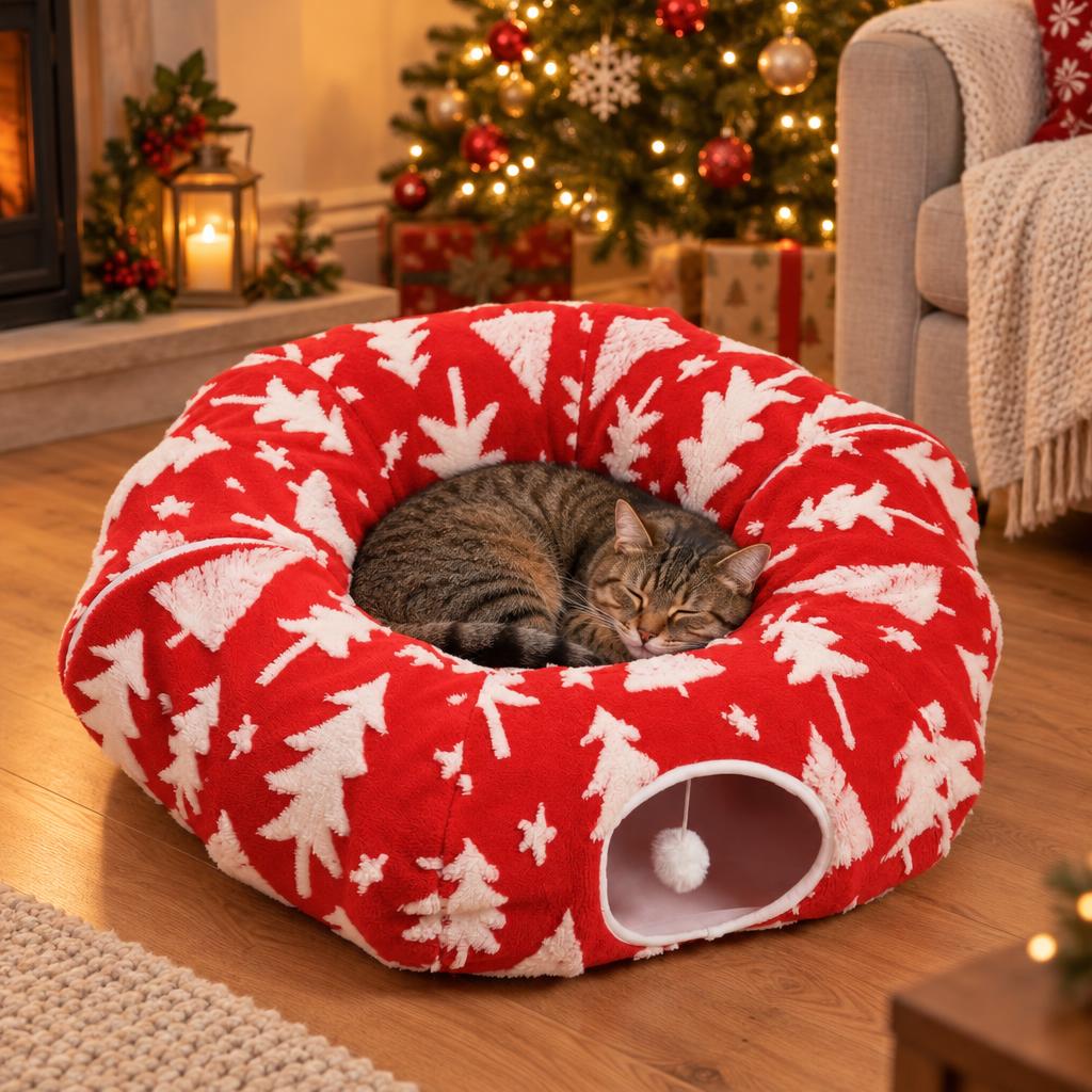 A tabby cat asleep in the red Christmas-tree cat tunnel bed, zipped into its round donut shape, by a Christmas tree